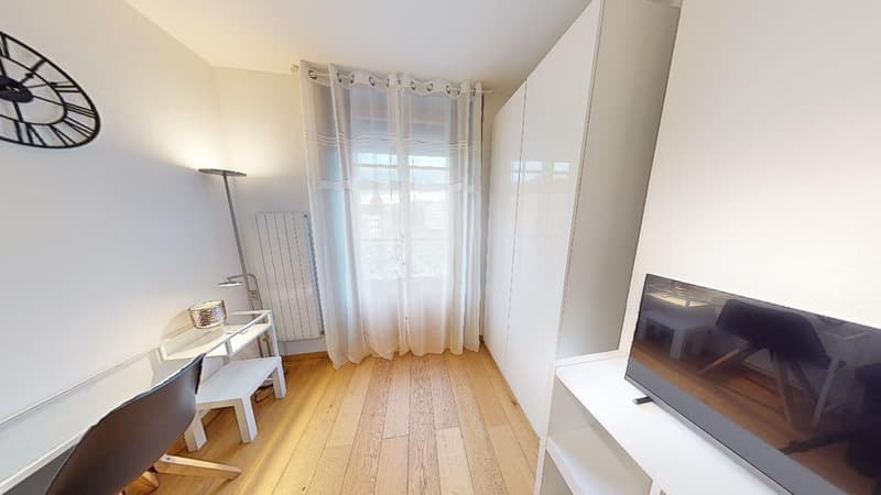 Spacious bedroom with hardwood floors, white walls, large windows with sheer curtains, wardrobe, desk, and a TV stand.
