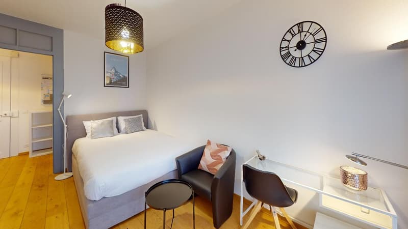 Bedroom with a double bed, a side table, a chair, a small desk, and a lamp