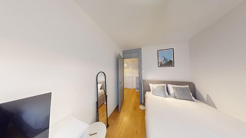 small bedroom with bed, mirror, small desk, and a television