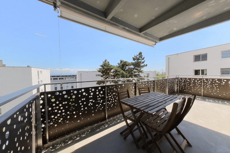Outdoor terrace with modern black metal railings, wooden table and chairs