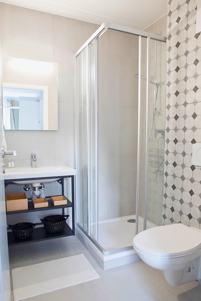 tiled floor, shower enclosure, white sink, toilet, wooden storage shelves, decorative baskets