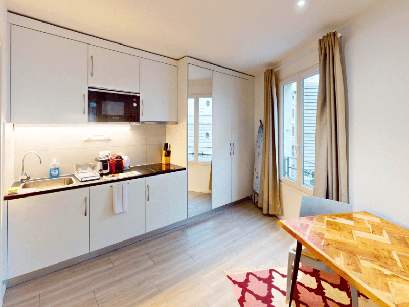 white cabinets, wooden countertop, stainless steel sink, microwave, electric kettle, toaster, dishwasher, wooden dining table, rugs, sliding glass door, balcony