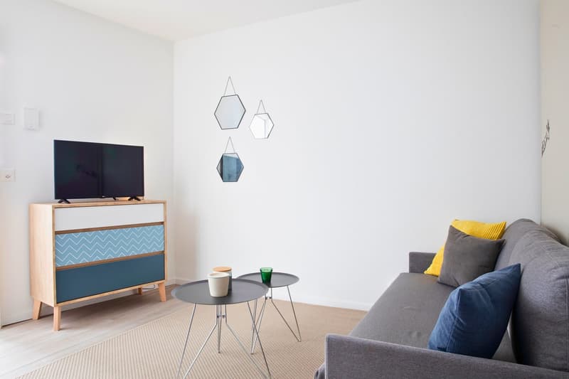 modern minimalist living room, gray couch, two side tables, blue cabinet, flat screen TV, wall decorations, carpet