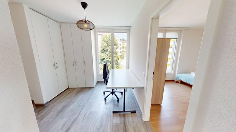 wooden floor, white walls, white cabinets, desk, chair, window with outdoor view, light fixtures, power outlet