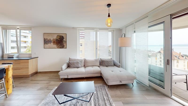 Modern living room with beige sectional sofa, coffee table, rug, kitchen bar, white walls, balcony with sea view, large glass windows