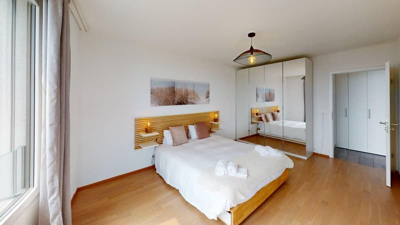 modern bedroom, wooden floor, white walls, large window, bed with white bedding, bedside shelves with lamps, large mirror, wardrobe