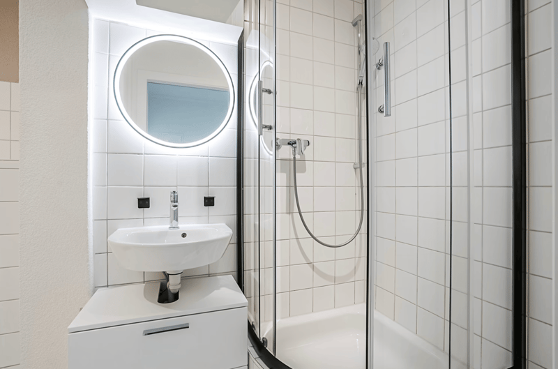 Bathroom: tiled walls, white sink, glass shower, faucet, showerhead, mirror, shower head, shower, power outlet
