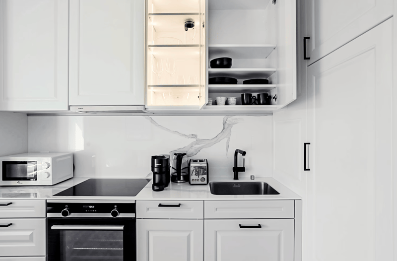 Modern, minimalist kitchen with white cabinets, marble backsplash, built-in oven, coffee maker, and dishwasher