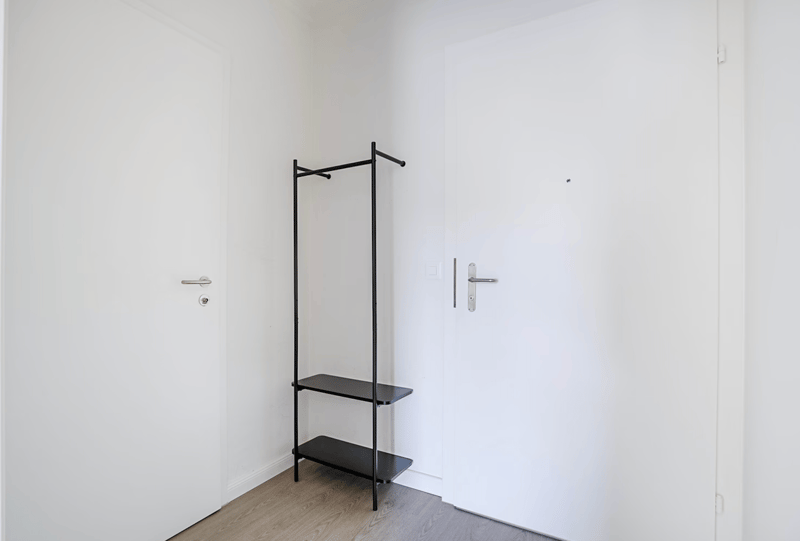 Minimalist room with a black metal clothing rack with two shelves, a white wall, and a wooden floor.