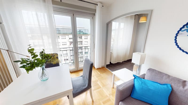 living room with white desk, gray chair, gray couch, blue pillow, white curtains, glass door leading to balcony, lamp, plant in vase