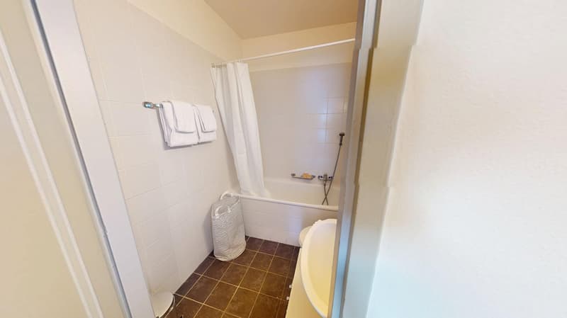 Bathroom with white tiles, bathtub, shower, toilet, towel rack, and a laundry basket.