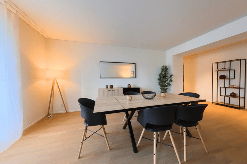 dining room, wooden floor, large wooden table, black chairs, white walls, small potted plant, cabinet, mirror, wooden floor lamp