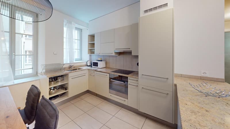 Modern kitchen with light-colored cabinets, built-in appliances including a dishwasher, granite countertops, and tile flooring. Large windows provide natural light.