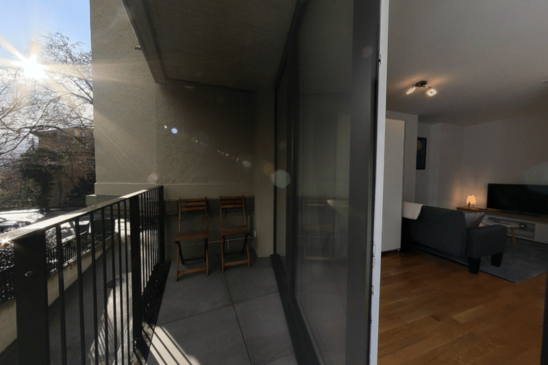 Balcony with chairs, indoor living area with sofa, table, lamp, and television