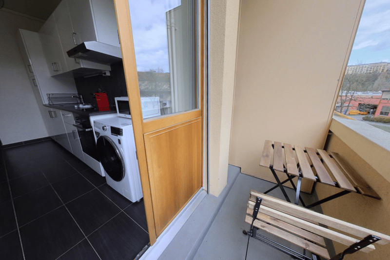 Apartment with a balcony, washing machine, and kitchen appliances visible through the open door