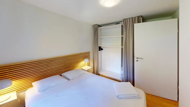 Spacious bedroom with wooden headboard, white bedding, closet, and curtains