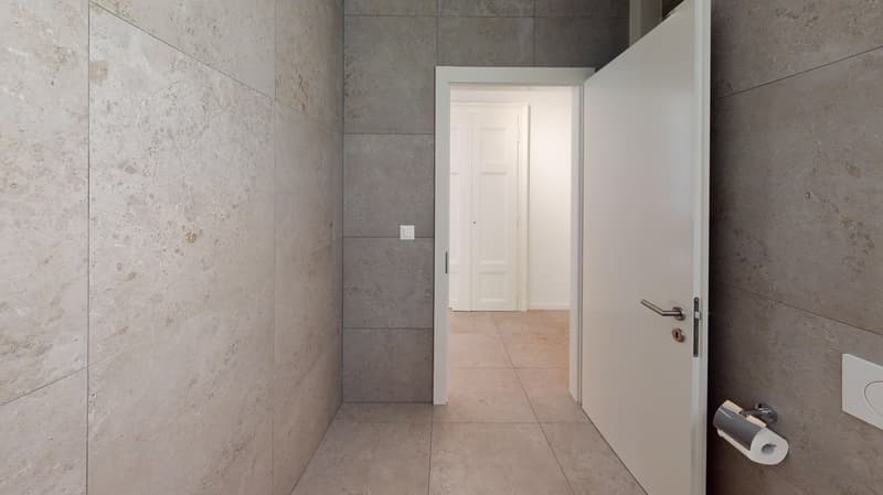 hallway with white door, white walls, gray tiled floor, power outlet