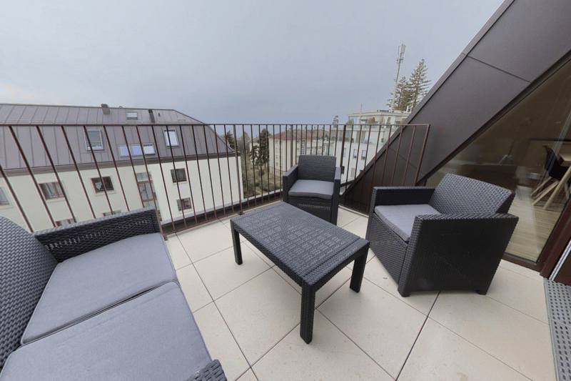 Balcony, three gray couches, black wicker coffee table, metal railings