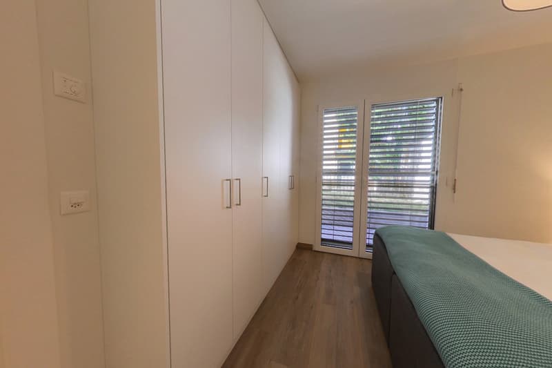 white walls, wooden floor, large white wardrobe, double bed, sliding glass door