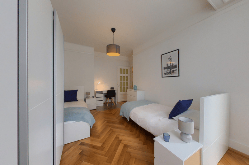 bedroom with two single beds, white bedding, white nightstands, ceiling lamp, desk with chair, picture on wall