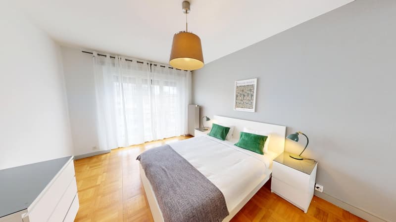 Bedroom with wooden floor, white walls, large bed, white nightstands, lamps, picture frame, and white curtains