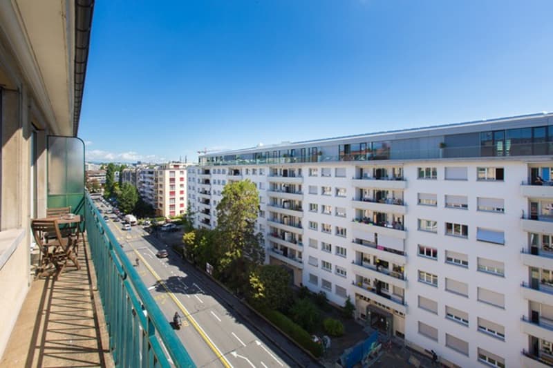 Balcony overlooking a road with traffic and trees, buildings with multiple windows