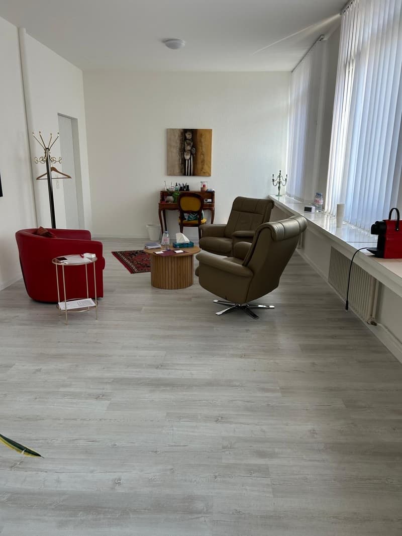 spacious living room with white walls, wooden floor, red and brown armchairs, wooden coffee table, rug, desk, radiator, white curtains