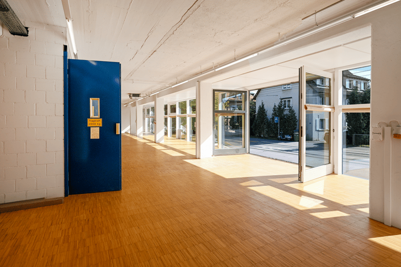 Bright room with wooden floors, white walls, sliding glass doors, and view of the street outside