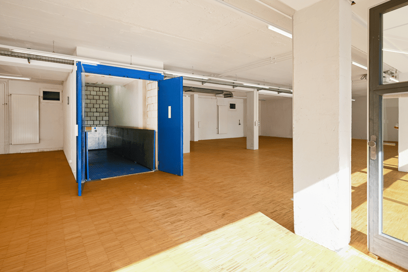 Empty room, wood floor, fluorescent ceiling lights, blue door leading to a staircase, white walls