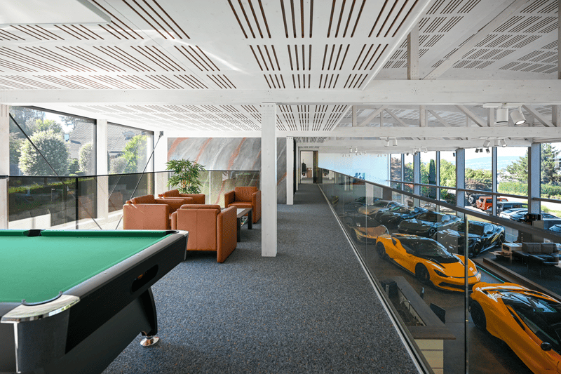 Ample glass windows, multiple sports cars on display, green billiard table, couches