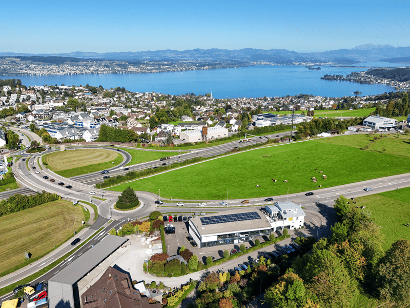 Aerial view of a town with buildings, large lake, highway, grass fields and mountains