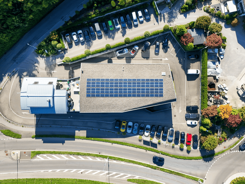 A building with a flat roof covered in solar panels, a large car park on the side.