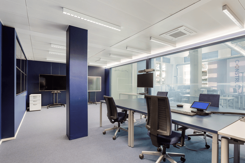 Empty office room with long table, monitors, chairs, and filing cabinet, modern design.
