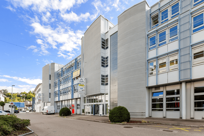 modern building, gray walls, windows, glass doors, bushes, van parked in front