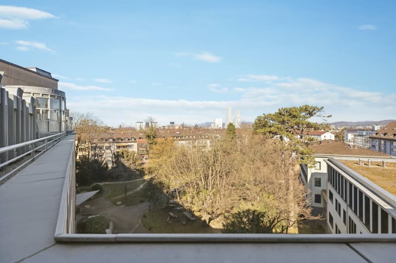 View from a balcony of an urban landscape with trees and buildings.