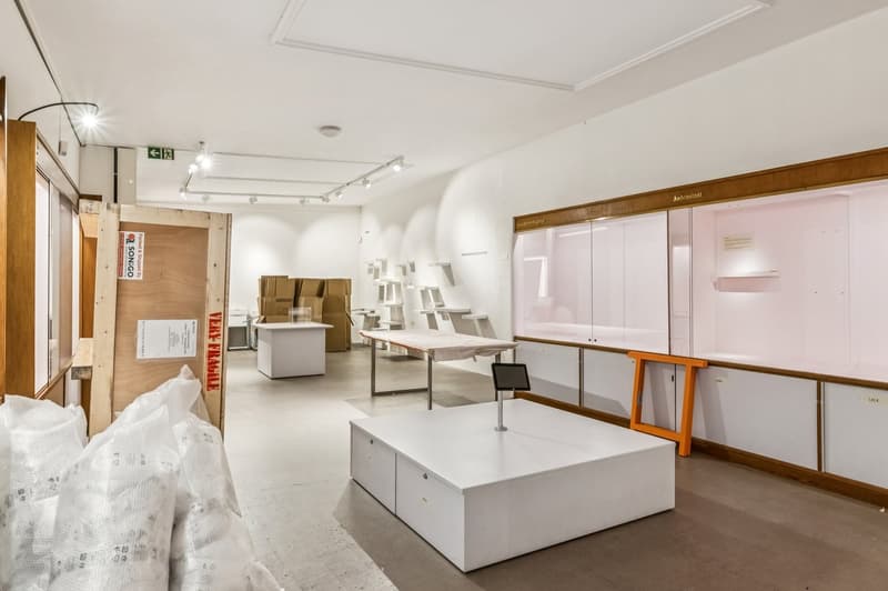 empty room, white walls, white ceiling, white floor, white tables, white cabinets, white display table, white display stand, white plastic bags, wooden door, wooden frames, lights on ceiling