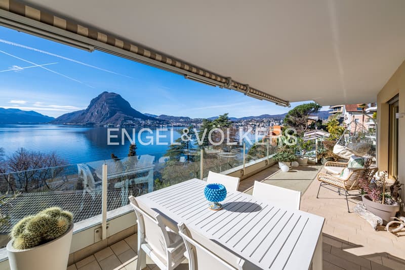 glass railing, large balcony, lake and mountain view, outdoor table and chairs, potted plants