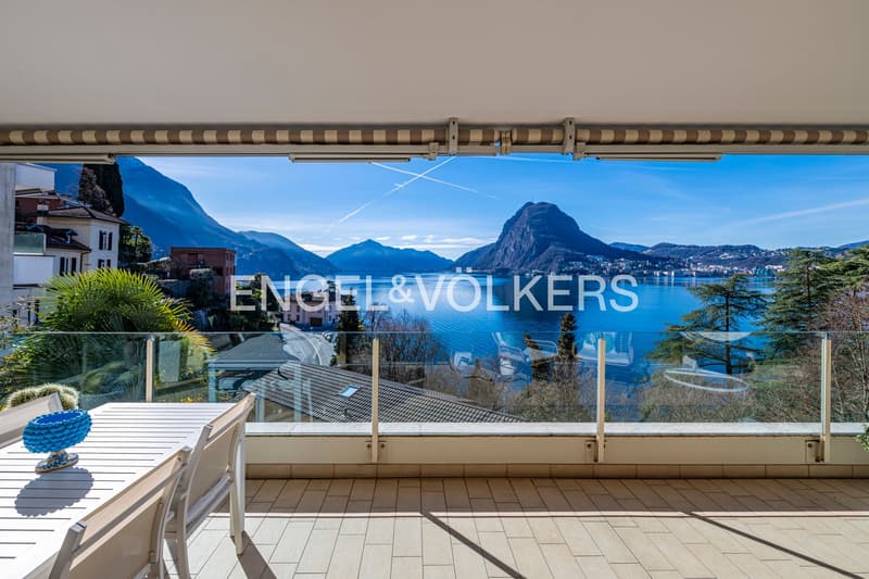 Balcony with table and chairs, glass railings, mountain view, clear blue sky