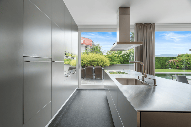 Modern kitchen, stainless steel countertops, silver cabinetry, double oven, gas range, glass door, sliding window, dining table, outdoor swimming pool