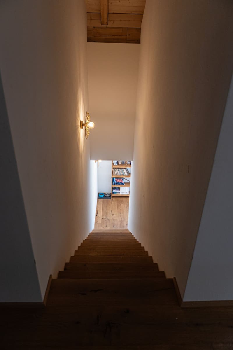 upward staircase with wooden steps and walls, light fixtures, a bookshelf in the corner