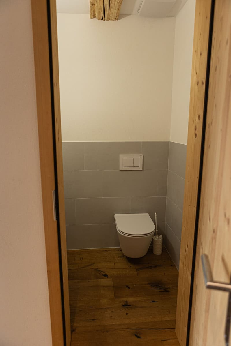 small bathroom with toilet, tiled walls, wooden floor, white walls