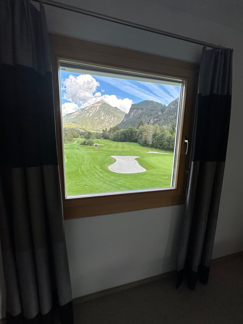 View from a window, with a golf course and mountains in the distance