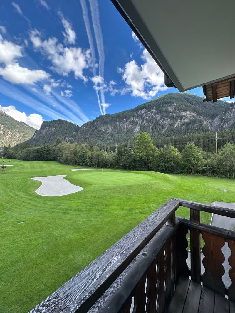 balcony with wooden railing, green golf field, mountains in the background