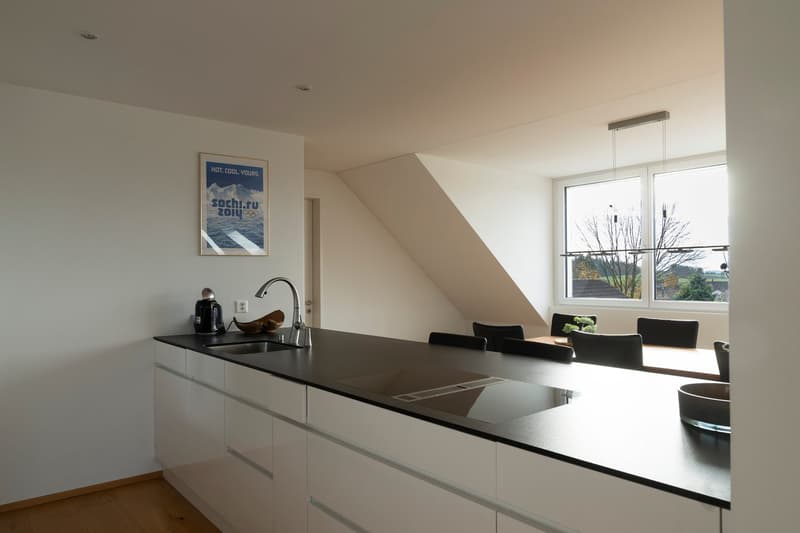 open kitchen with island, modern white kitchen, black countertops, white cabinets, electric kettle, silver faucet, 6 black chairs, window with view, suspended lamps