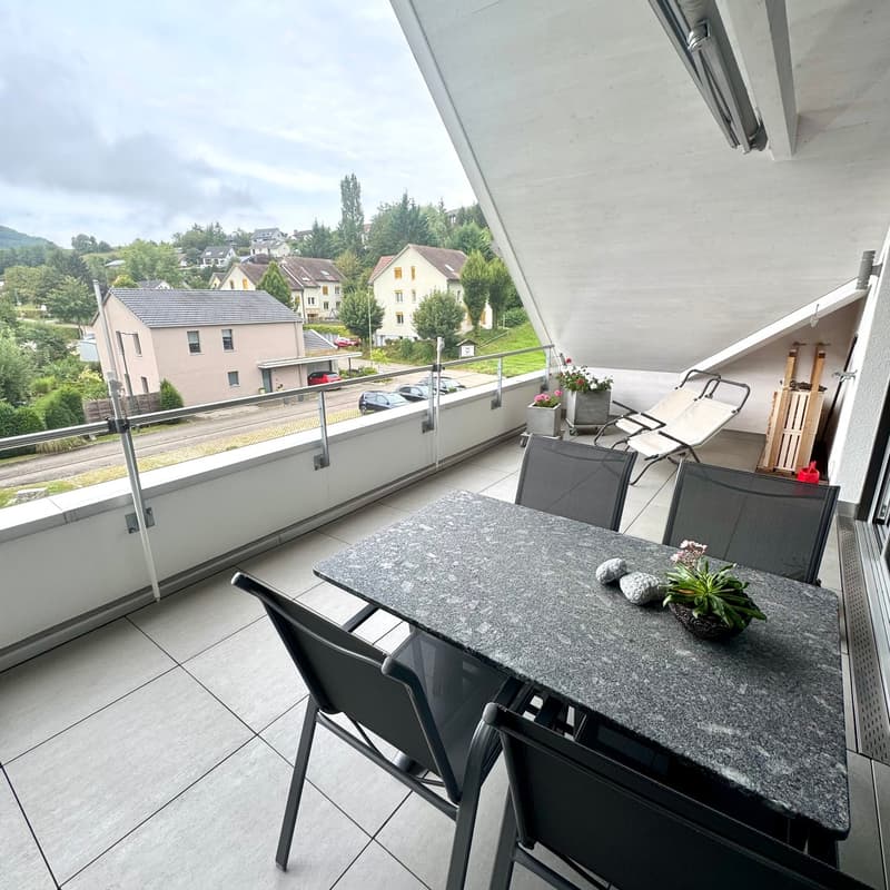 Table with chairs, tiled floor, railings, plants, distant houses and hills in the background