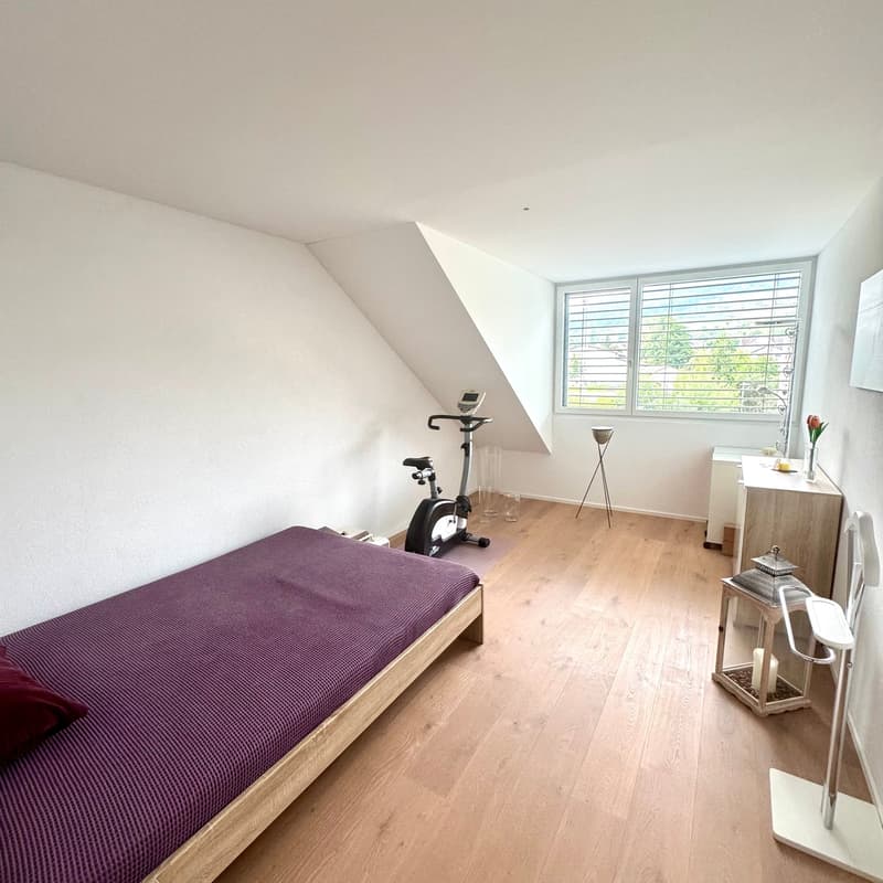 Single bed, wooden floor, wall mounted speaker, stationary bike, lamp, small dresser, rose, window with blinds, slanted ceiling