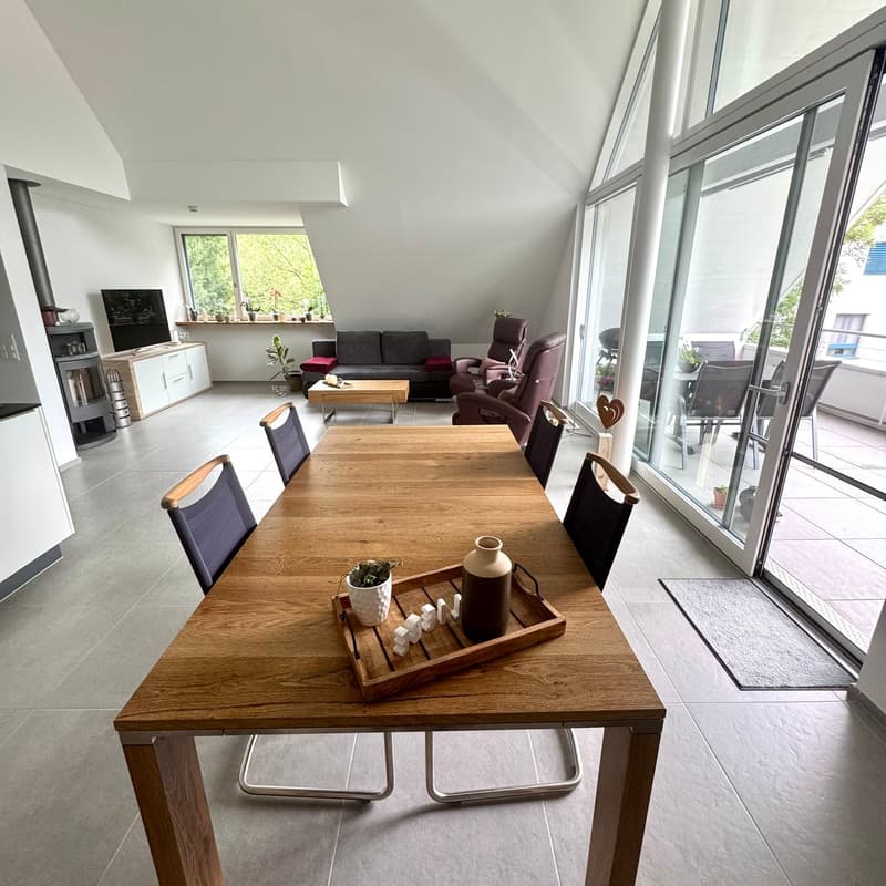Dining area, large windows, modern wooden table, chairs, potted plants, living room with sofa, coffee table, recliner chairs, fireplace, TV, and kitchen area with stove, cabinet.