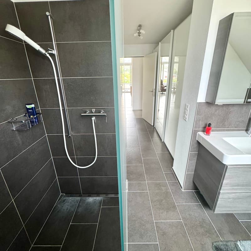 tiled floor, tiled walls, glass shower, metal showerhead, shampoo holder, vanity, sink, mirror, hallway with windows