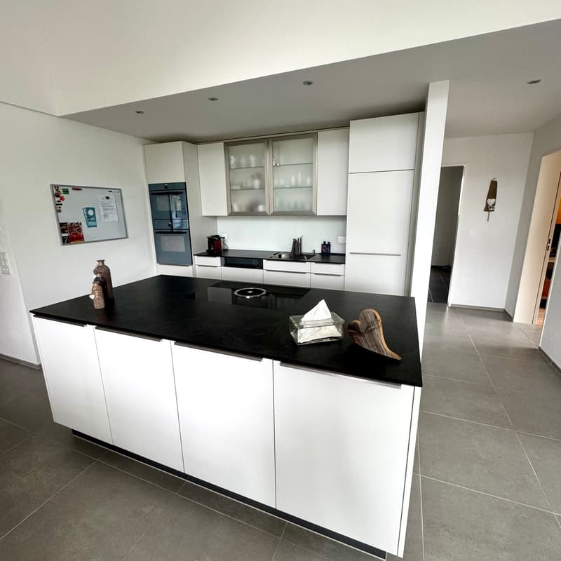 Open-plan kitchen, dark granite countertop, white cabinetry, black gas stove, modern design, white walls, gray tiles