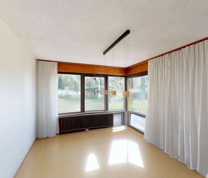 Large windows with white curtains, white walls, wooden floor, black ceiling lamp, view to the outside
